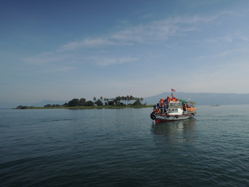 A passenger boat operates in the serene morning at Toba Lake